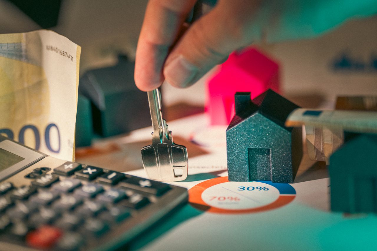 A close-up of real estate financial planning with keys, calculator, and money.